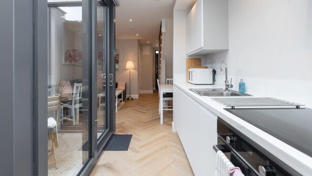 Een moderne keuken met een groot eiland, een magnetron en een spoelbak. Een eethoek met een tafel en stoelen is zichtbaar door een glazen deur.
