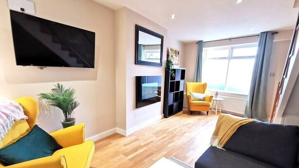 A modern living room with a flat-screen TV mounted on the wall, a yellow armchair, a dark sofa, and a small table with a plant.