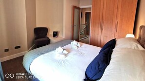A hotel room with a large bed, a wooden wardrobe, a chair, and a hanging light fixture.