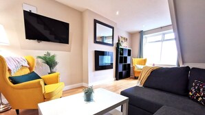 A modern living room with a flat-screen TV, yellow armchairs, a dark sofa, and a white coffee table.