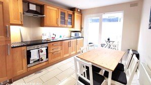 A modern kitchen with wooden cabinets, a stainless steel oven, a microwave, and a dining area with a wooden table and white chairs.
