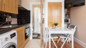A compact kitchen with a washing machine, a microwave, and a dining area with a table and chairs. - *COSY 2BED APARTMENT*FAST WIFI*&TV*TRENDY RANELAGH (Dublin 6)