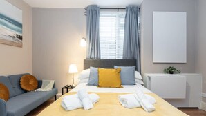 Ein modernes Hotelzimmer mit Bett, Sofa, Nachttisch, Lampe und einem Fenster mit Vorhängen.
