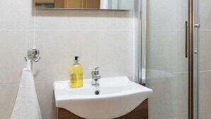 Ein Badezimmer mit einem weißen Waschbecken, einem Spiegel und einer Duschkabine aus Glas.
