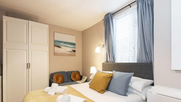 Ein Hotelzimmer mit Bett, Nachttisch, Lampe, einem Gemälde und einem Fenster mit Vorhängen.
