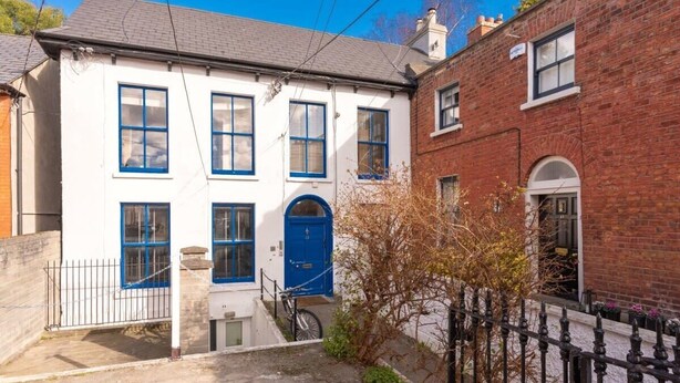 Uma casa de dois andares com fachada branca e detalhes em azul, apresentando uma porta azul central e várias janelas.