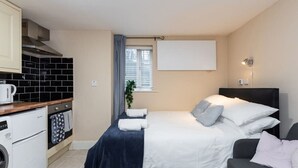 Quarto compacto com cama, mesa de cabeceira e pequena cozinha.