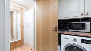 Cozinha compacta com micro-ondas, máquina de lavar Bosch e armários brancos.