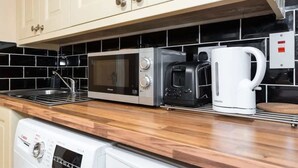 Uma cozinha com micro-ondas, torradeira e máquina de café sobre um balcão de madeira, lava-louças abaixo e painel de azulejos.