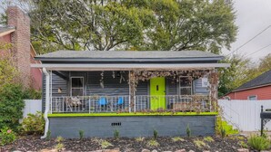 Une maison de plain-pied avec un porche, une porte verte et un petit jardin.