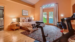 Une chambre à coucher comprenant un lit, un tapis de course, un bureau et une fenêtre donnant sur une clôture verdoyante.