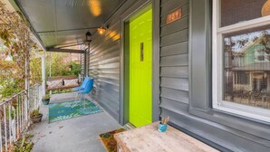 Un porche abrité avec une porte vert vif, un banc et une chaise bleue.