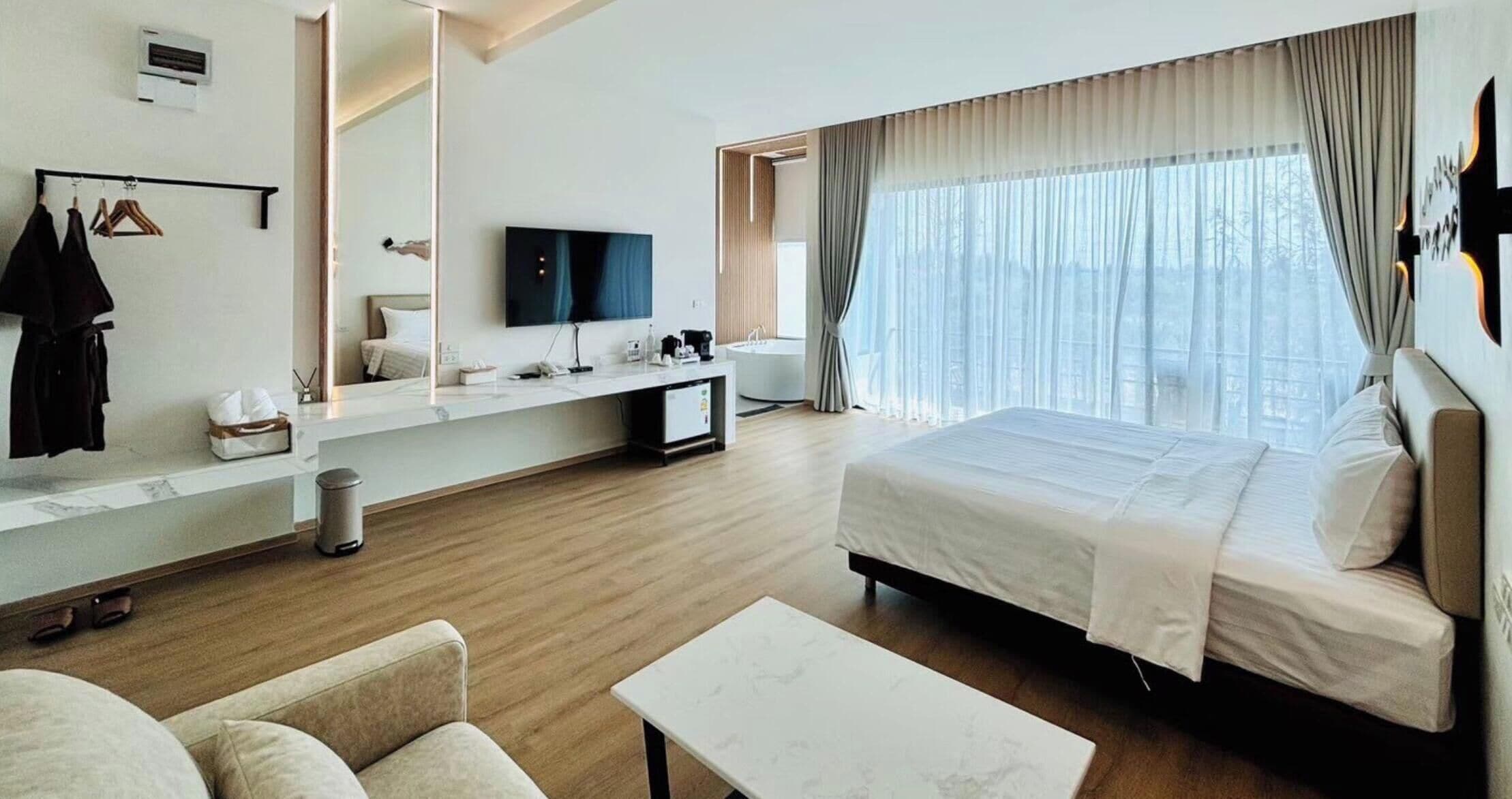 A modern hotel room with a large bed, a TV, a desk, and a bathroom.