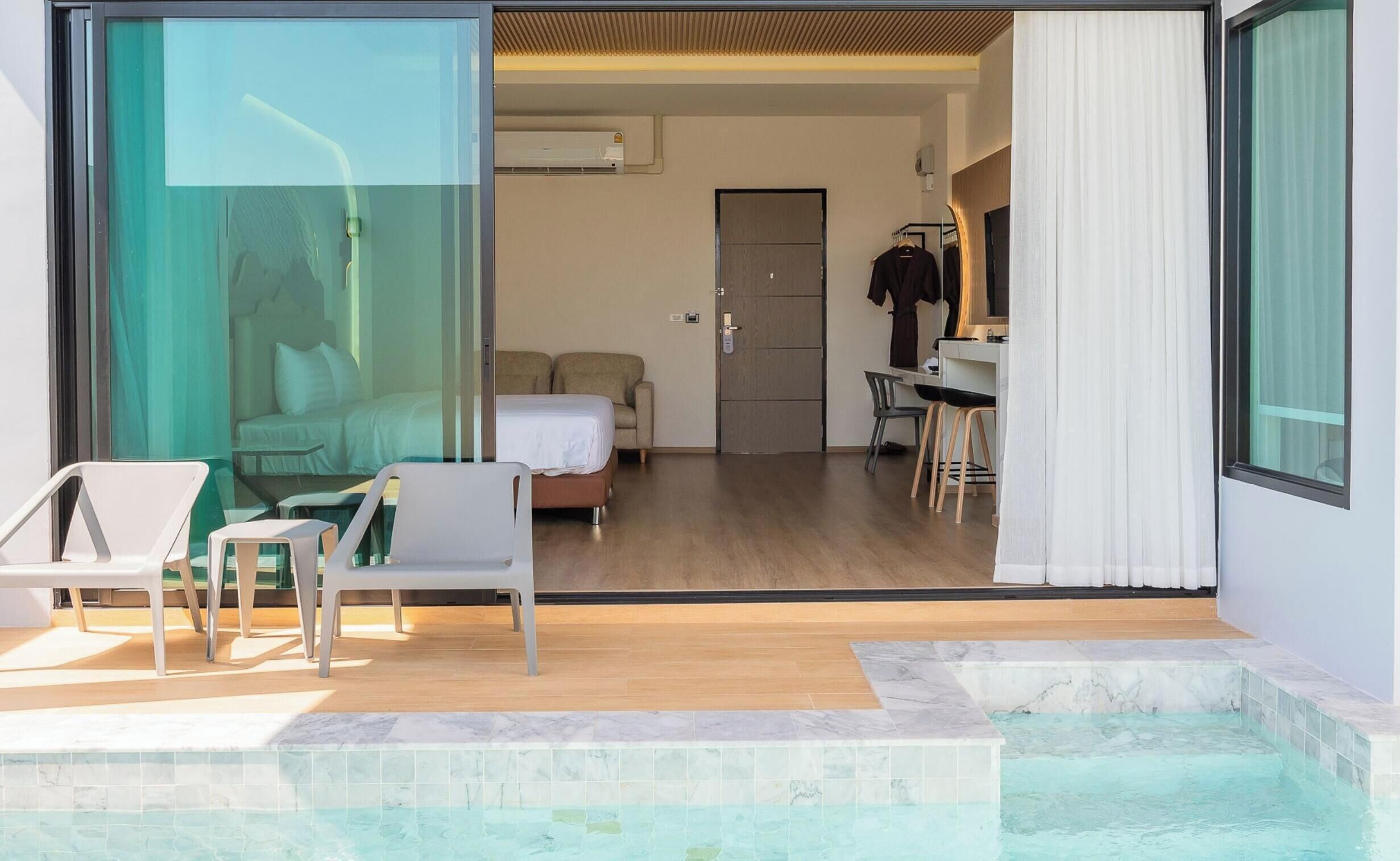 Ein modernes Hotelzimmer mit Glastür zu einem Balkon, einem Bett, einem Schreibtisch und einer Duschkabine.