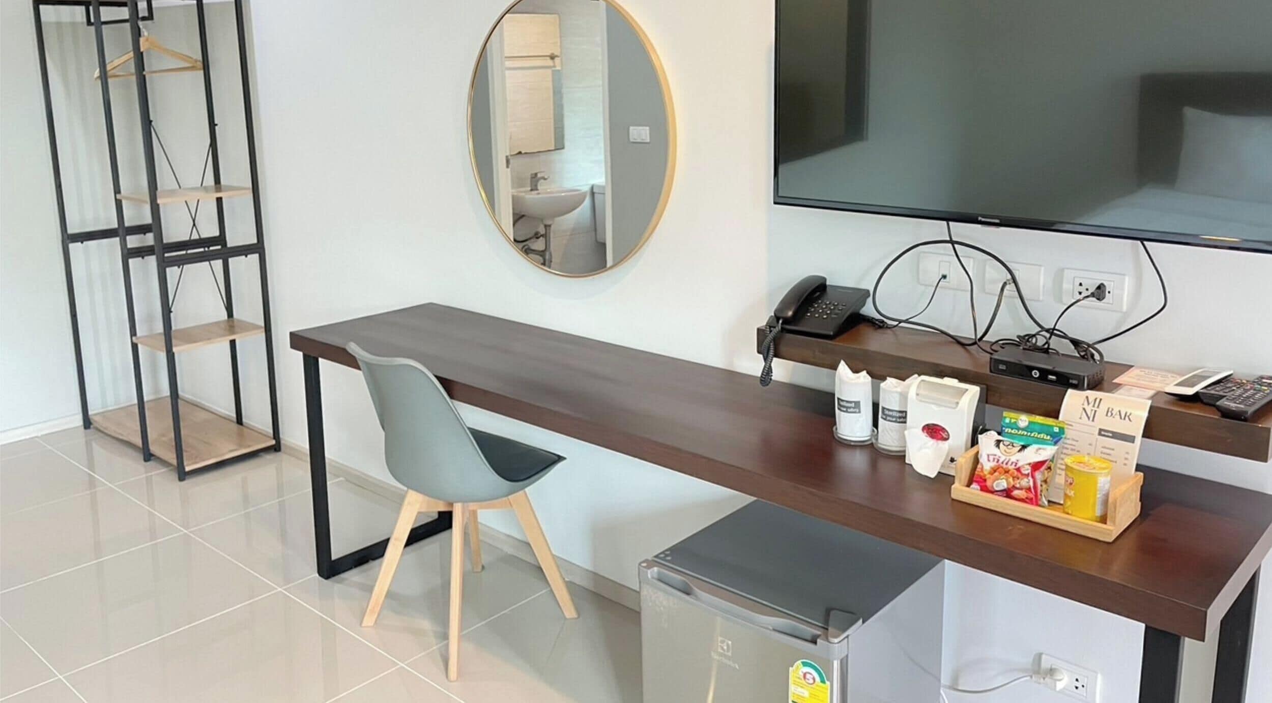 A modern hotel room with a desk, chair, minibar, and a large TV.