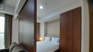 Una habitación de hotel con una cama, un armario de madera, una mesita de noche con lámpara y un sofá.