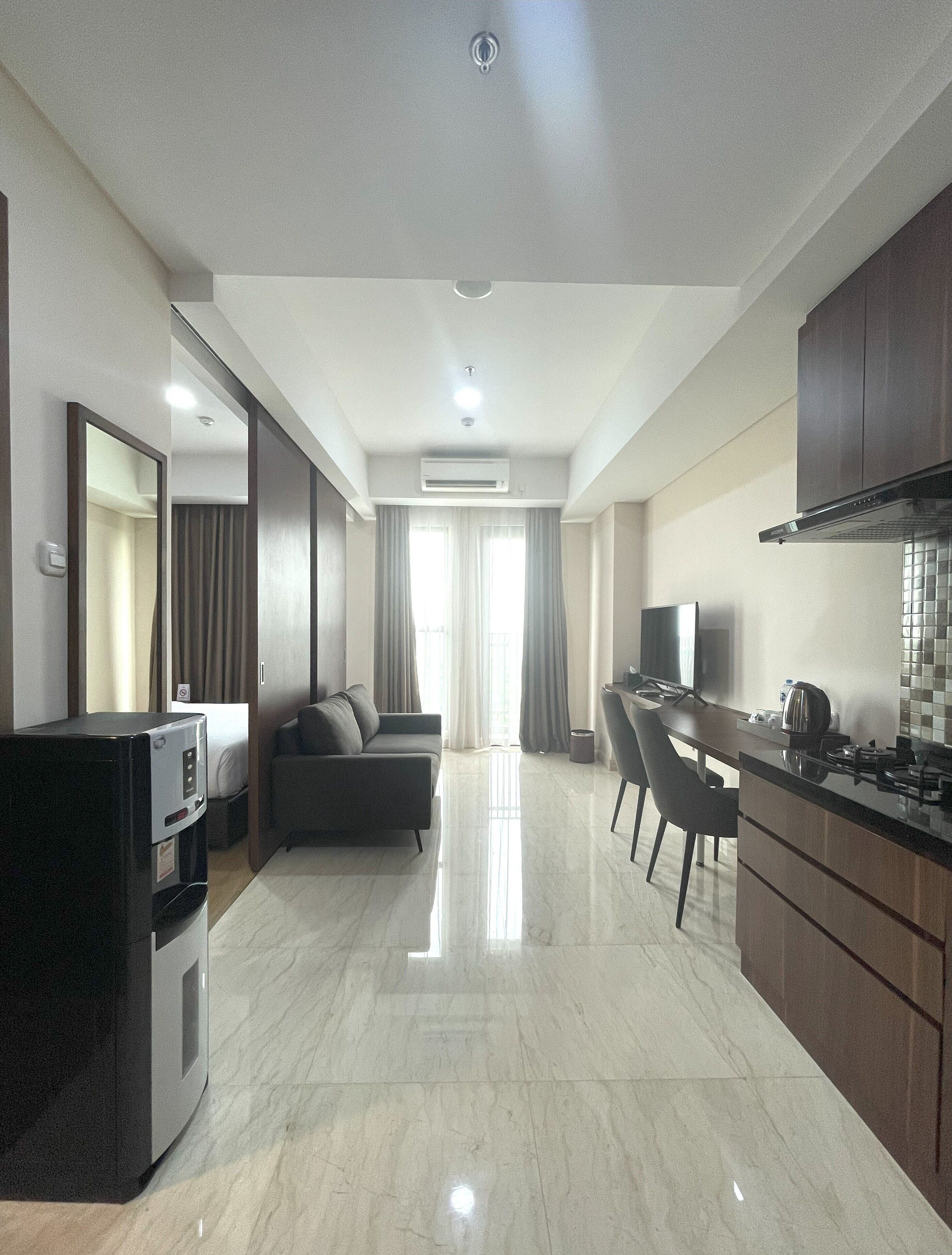 A modern hotel room with a kitchenette, a sofa, a dining table, and a TV.