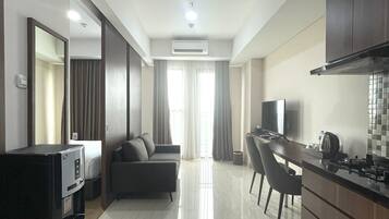 A modern hotel room with a kitchenette, a sofa, a dining table, and a TV.