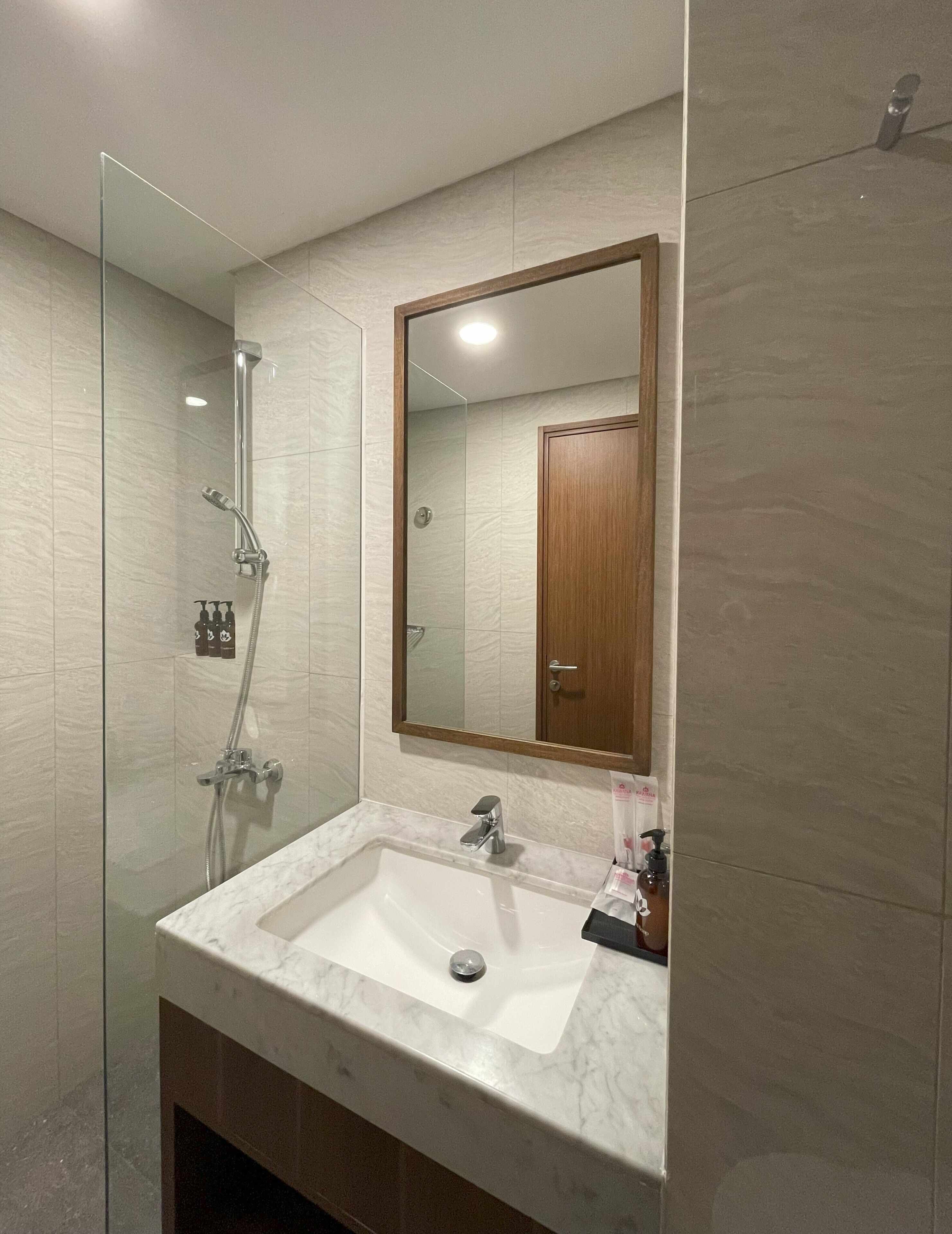 A bathroom with a glass-enclosed shower, a marble sink, and a wooden door.