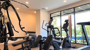 Un gimnasio moderno con diverso equipo de ejercicio, amplias ventanas y vistas a zonas verdes.