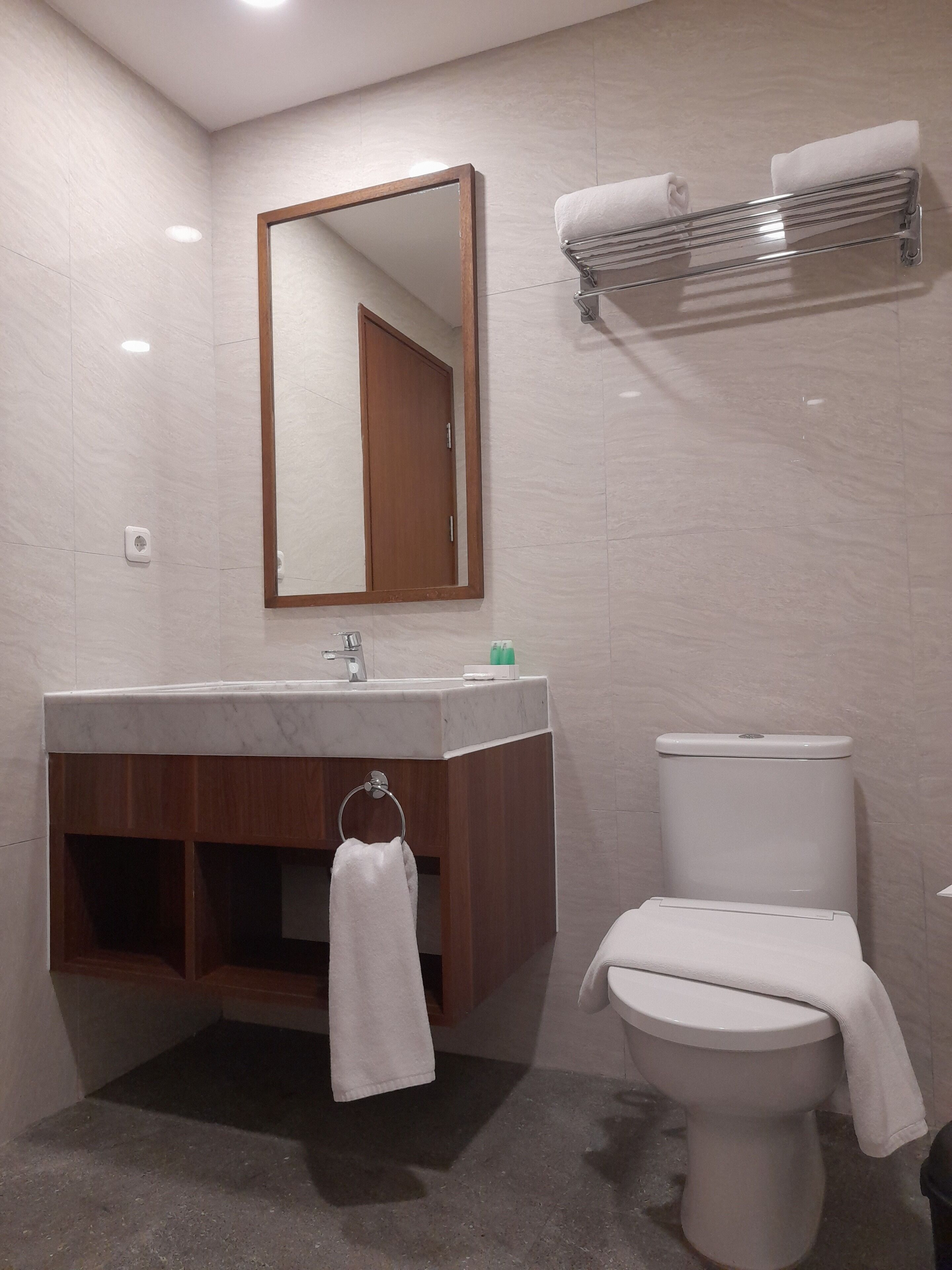 Et moderne badeværelse med en marmorvask, en trækommode, et toilet, et håndklædestativ og et spejl.