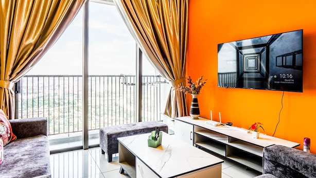 Een moderne woonkamer met een groot raam, een bank, een salontafel en een flatscreen-tv aan een oranje muur.