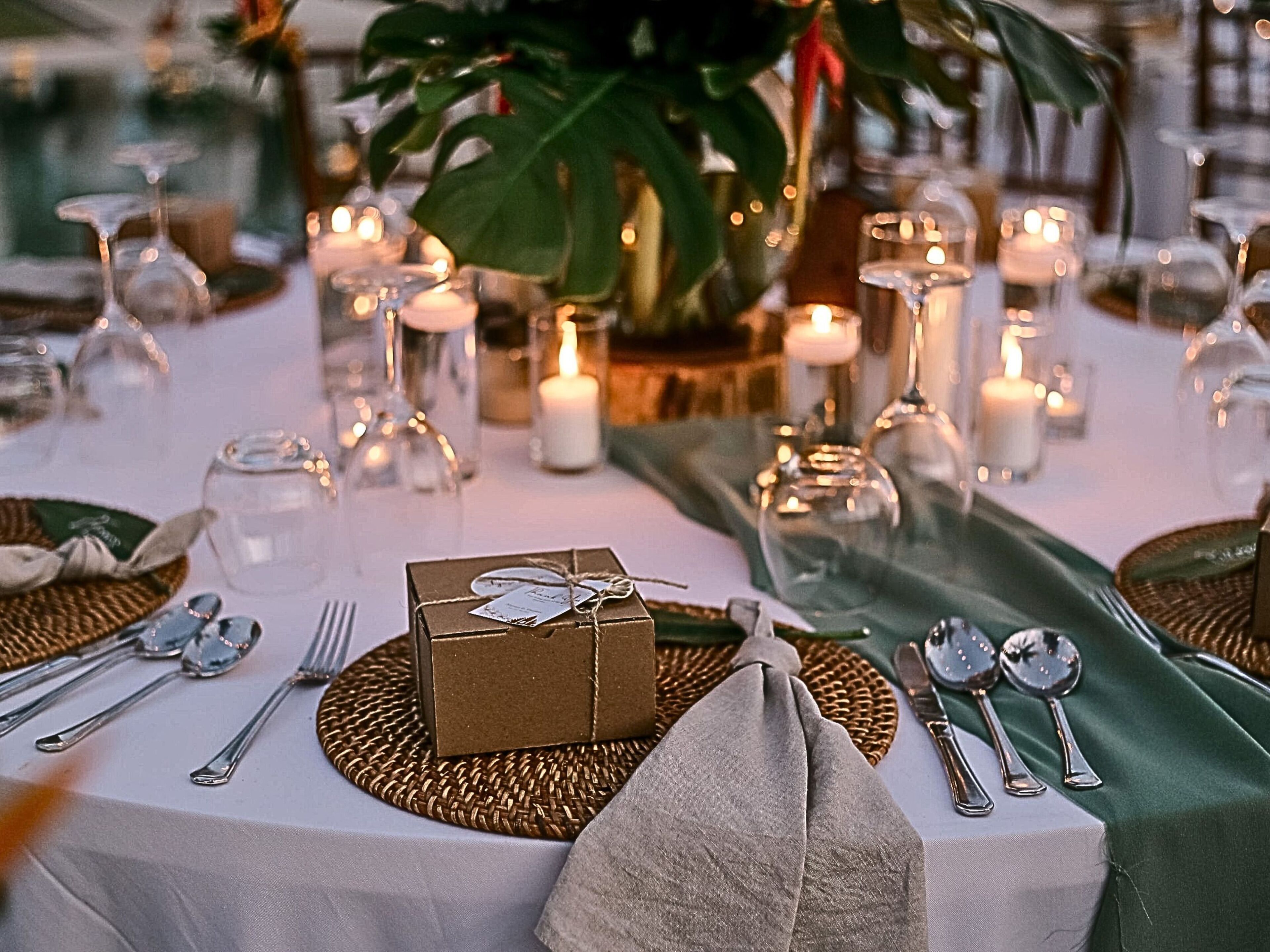 A table set for a meal with candles, a gift box, and a green table runner.