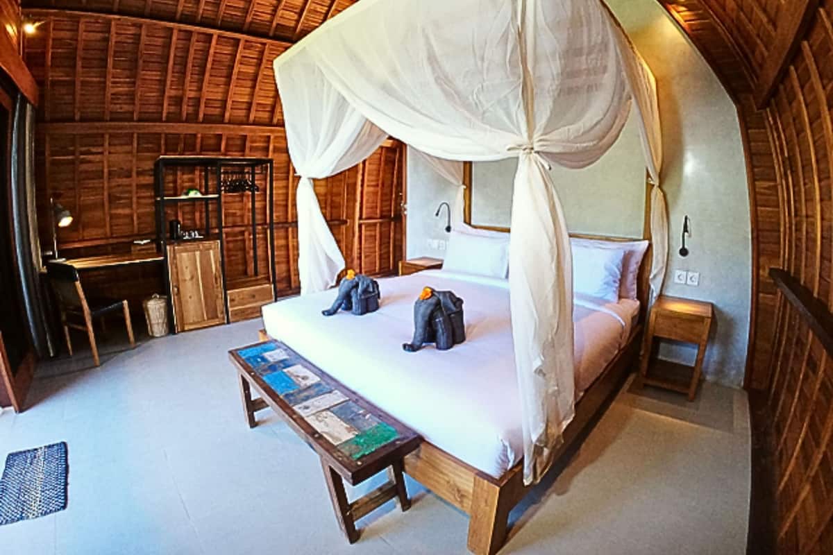 A room with a four-poster bed, a wooden desk, and a small table with a book.