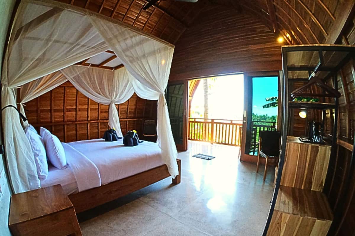 A wooden room with a bed, a bench, and a balcony with a view.