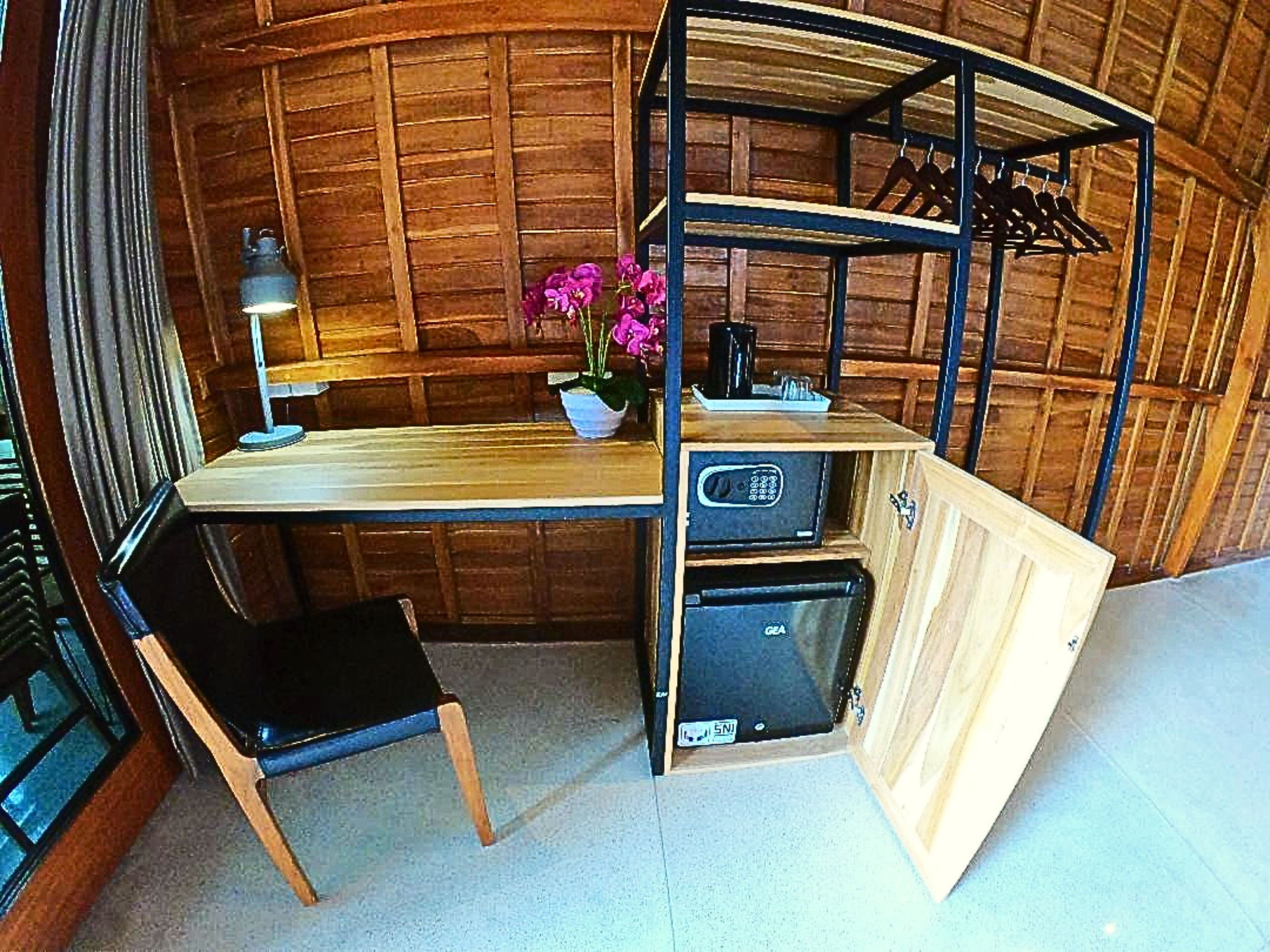 A compact, rustic room with a wooden desk, a chair, a small shelf with a potted plant, and a built-in safe.