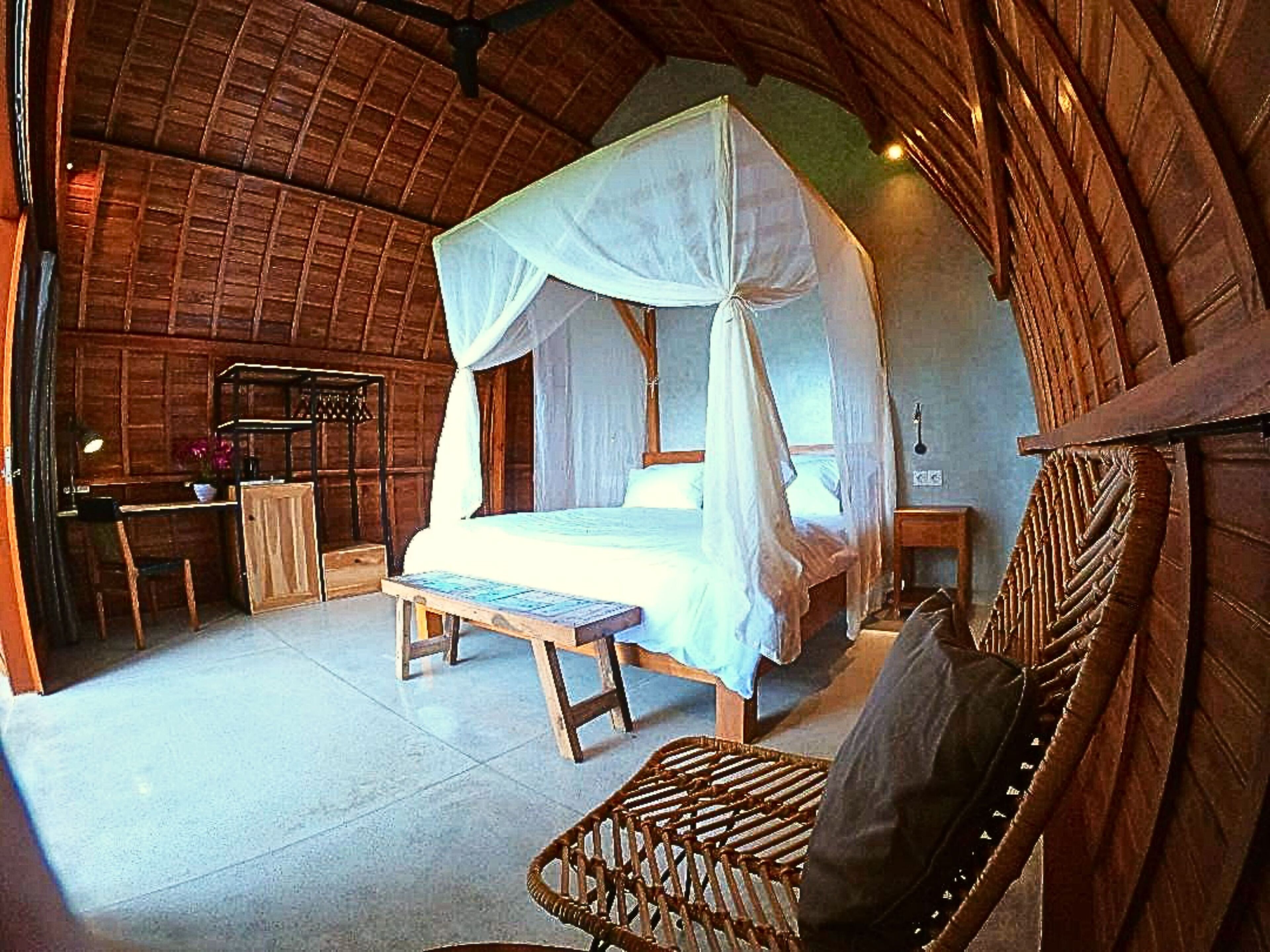 A rustic bedroom with a four-poster bed, a wooden desk, and a wicker chair.