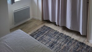 Une pièce avec une grande fenêtre, un radiateur, un plancher en bois et un rideau.