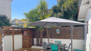 An outdoor patio with a table and chairs, a wooden deck, and a covered area with a wooden fence and plants. - Cozy Triplex Apartment with Terrace Near Beach in Arcachon (Arcachon)