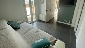 A bedroom with a bed, a green pillow, a TV, and a sliding glass door leading to a balcony. - Cozy Triplex Apartment with Terrace Near Beach in Arcachon (Arcachon)