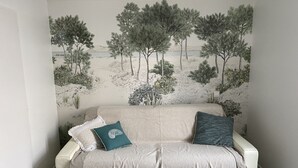 A room with a white sofa, two pillows, and a wall mural of trees and landscape. - Cozy Triplex Apartment with Terrace Near Beach in Arcachon (Arcachon)