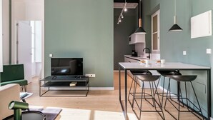 Et moderne opholdsrum med fjernsyn, siddepladser, køkken og barstole.