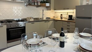 A modern kitchen with a gas stove, oven, and stainless steel appliances. There is a dining table set with wine glasses and plates. - Uffizi SuiteLarge and elegant renovated apartment in the heart of Florence (Firenze)