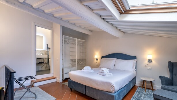 A bedroom with a bed, bedside tables, a chair, a walk-in closet, and a skylight. - Uffizi SuiteLarge and elegant renovated apartment in the heart of Florence (Firenze)