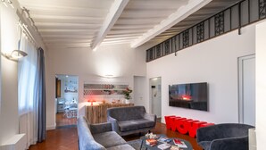 A modern living room with a sofa, armchairs, a coffee table with books, a TV, and a staircase. - Uffizi SuiteLarge and elegant renovated apartment in the heart of Florence (Firenze)