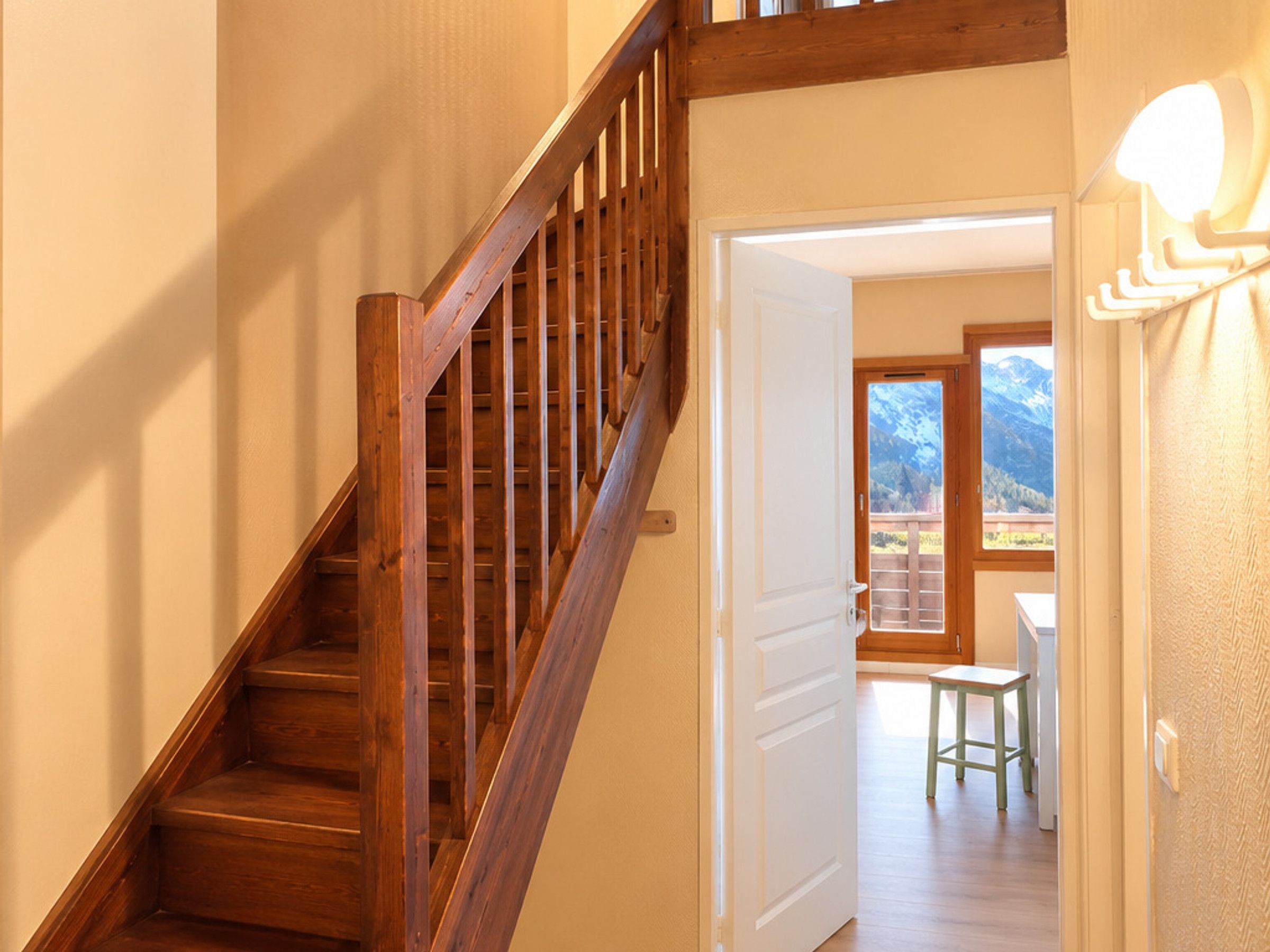 A wooden staircase leading to a room with a view of mountains through a door.