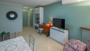 A room with a bed, a desk with a TV, a chair, a lamp, and a radiator. - Air-conditioned studio, quiet, Menton center, terrace (Menton)