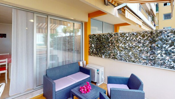 A balcony with wicker furniture, a glass door, and a decorative wall. - Air-conditioned studio, quiet, Menton center, terrace (Menton)