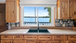 A kitchen with wooden cabinets, a double sink, and a view of a lake.