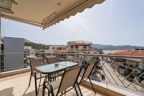A balcony with a table and chairs, overlooking a cityscape with buildings and a body of water.