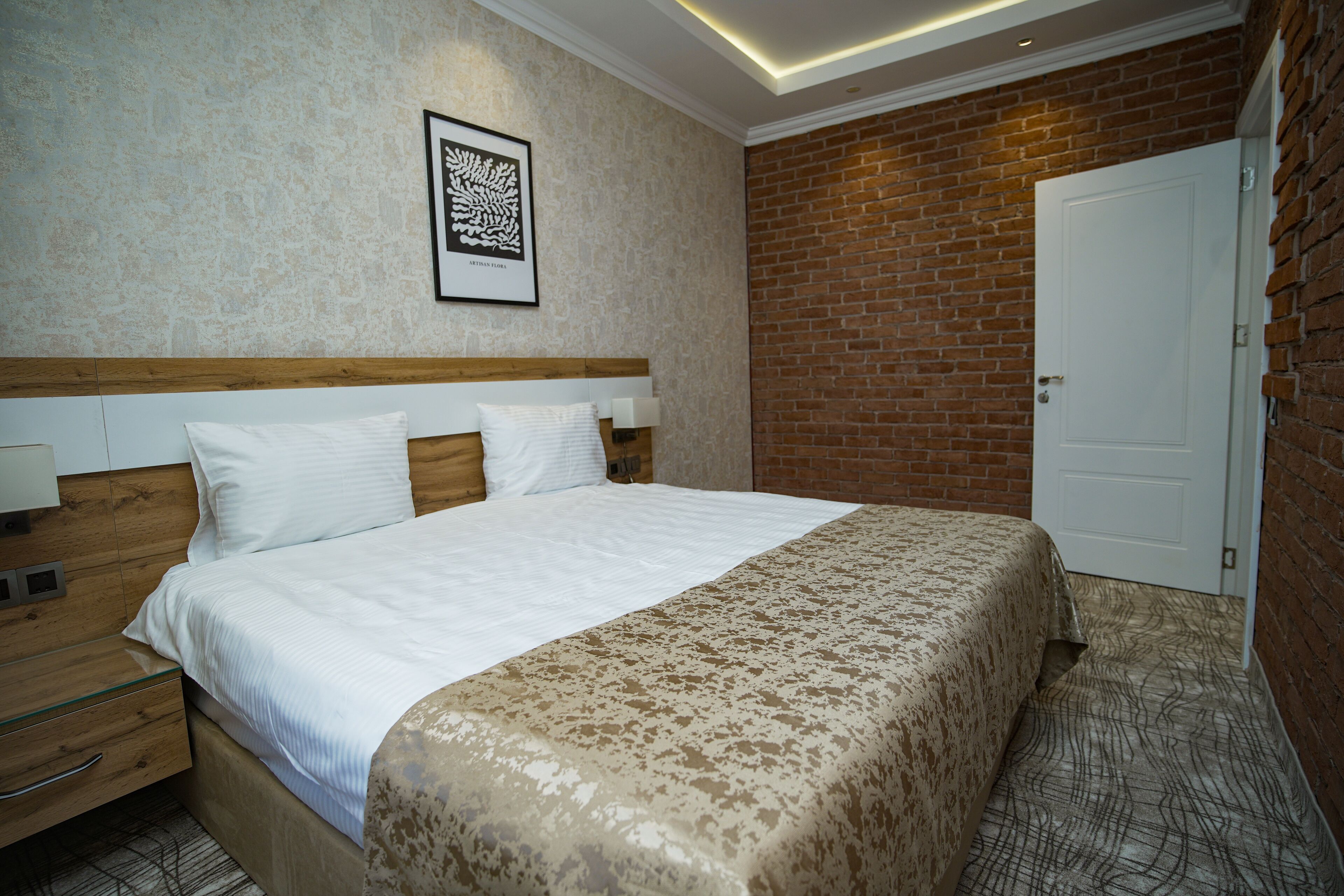 Una camera d'albergo con una testiera in legno, un letto grande con copriletto decorato, una porta bianca e una parete in mattoni.
