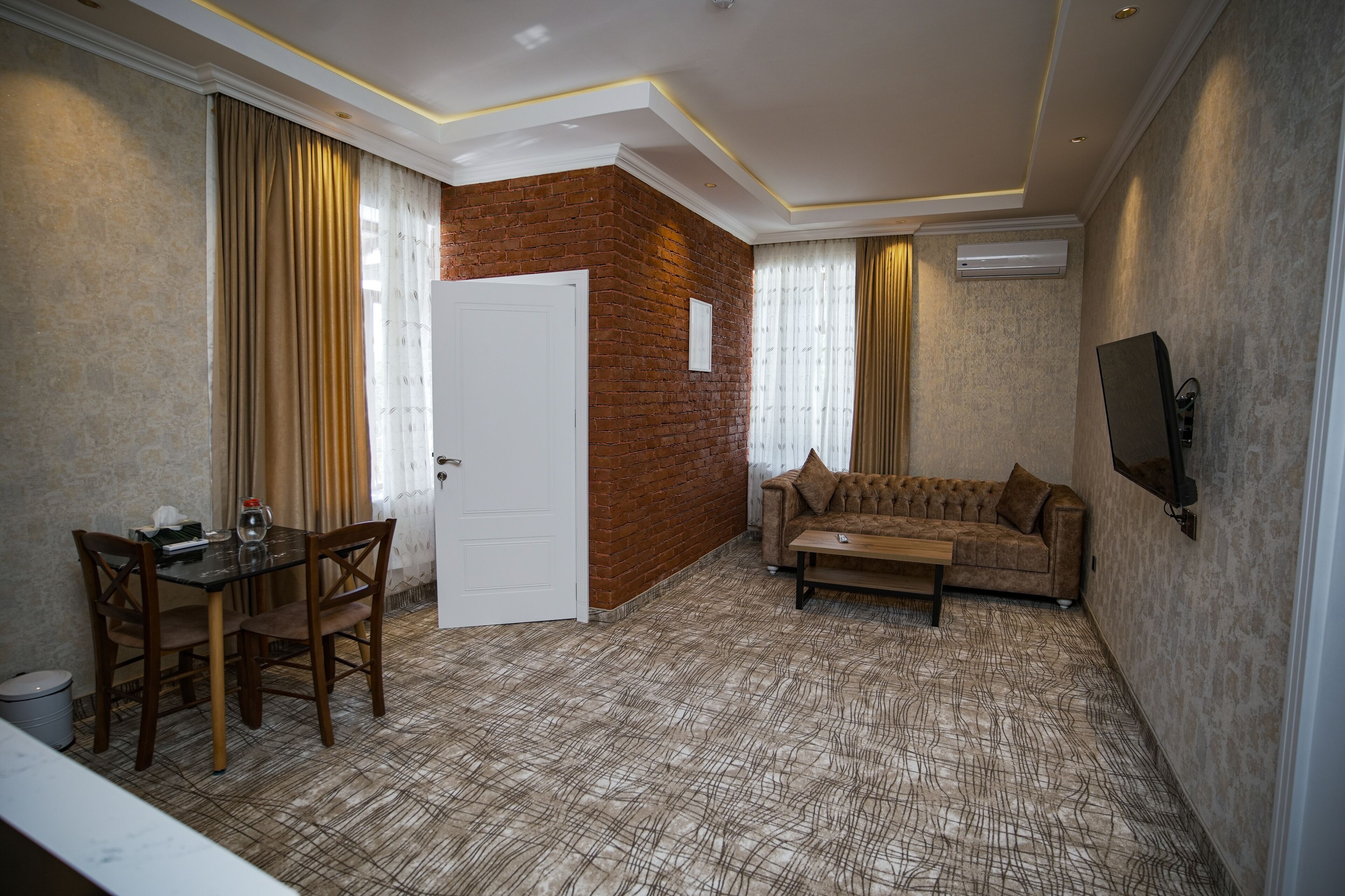 Una habitación con una pared de acento de ladrillo, un sofá, una mesa de centro, un televisor montado en la pared y una zona de comedor con sillas y una mesa.