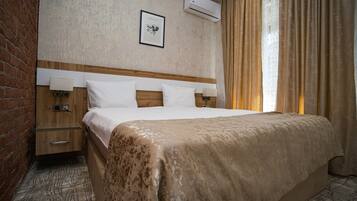 A hotel room with a large bed, two bedside tables, a wooden headboard, a wall-mounted air conditioner, and a framed picture.