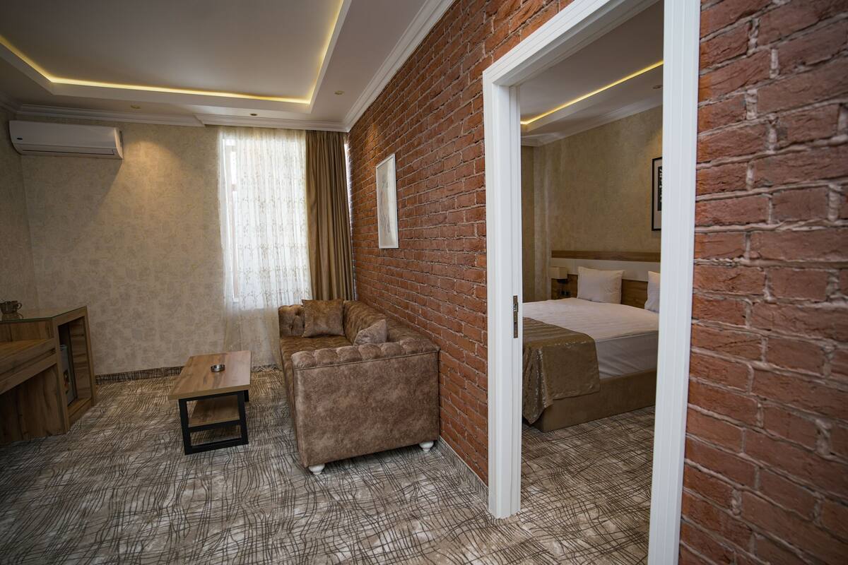 Quarto de hotel com parede de tijolos, uma cama, um sofá, uma mesa pequena e uma escrivaninha.