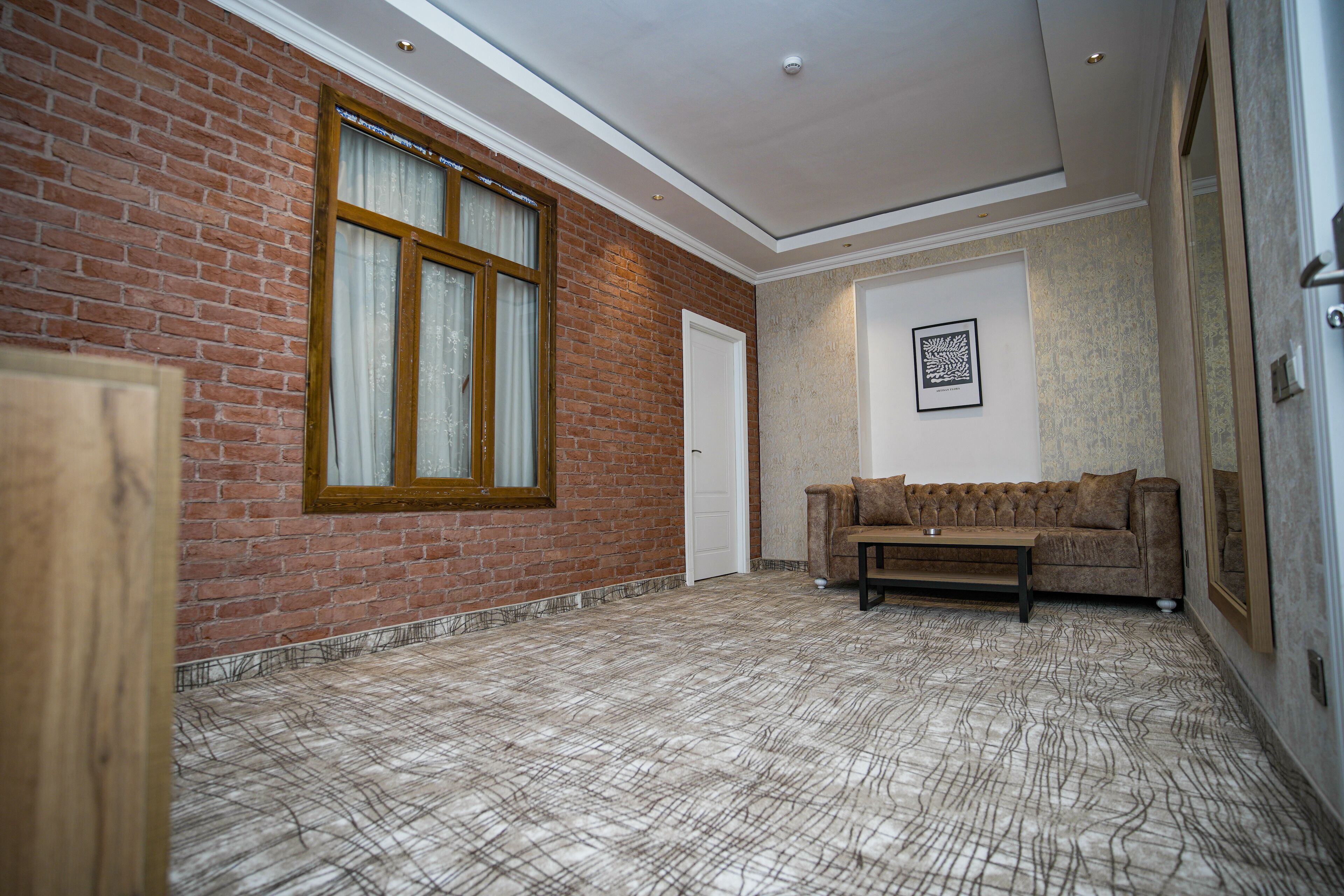 A room with a brick wall, a large window with curtains, a brown sofa, and a patterned floor.