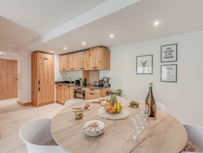 Una cocina moderna con armarios de madera, una mesa de comedor dispuesta con platos, vasos y una cesta de fruta.